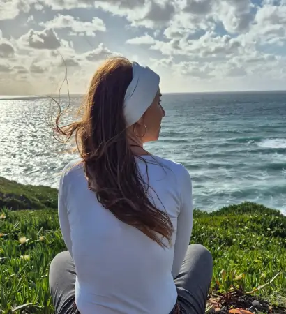 Frau mit langen Haaren sitzt am Meer und blickt in die Weite – Symbol für Ruhe, Reflexion und persönliche Entwicklung.