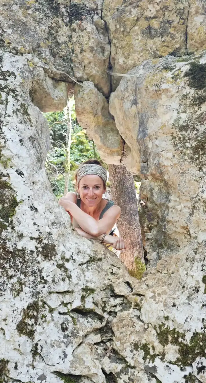 Frau lächelt durch eine Felsöffnung, umgeben von Natur und warmem Licht – Moment von Lebendigkeit und Verbundenheit mit der Umgebung.