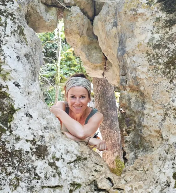 Frau lächelt durch eine Felsöffnung, umgeben von Natur und warmem Licht – Moment von Lebendigkeit und Verbundenheit mit der Umgebung.